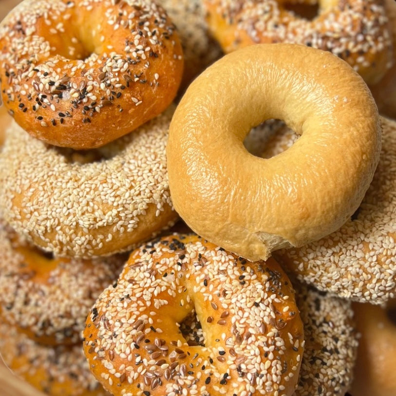 Assorted bagels including plain, sesame seed, and everything bagel on a wooden surface.